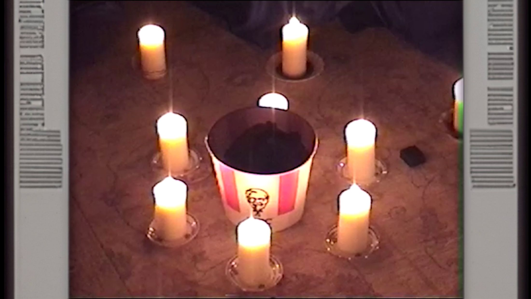 Still from DreamArena (2024) by Melle Nieling, a bucket of KFC surrounded by a ring of candles