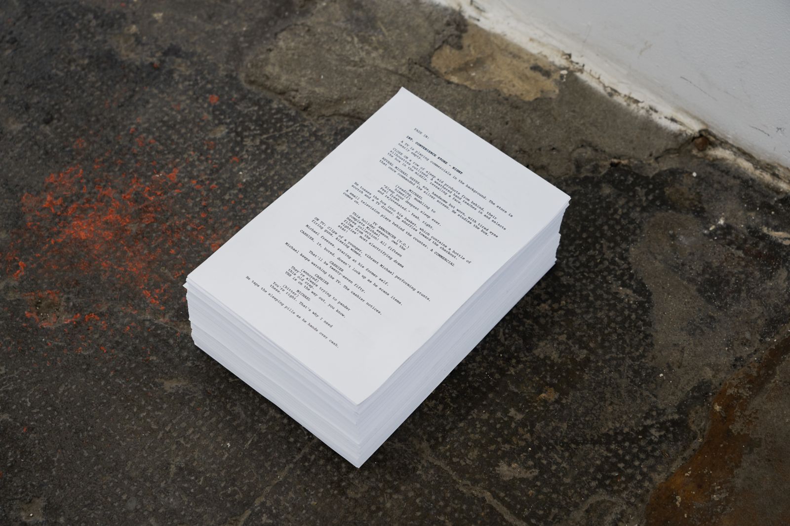 A stack of papers with a screenplay printed on it on a worn concrete floor