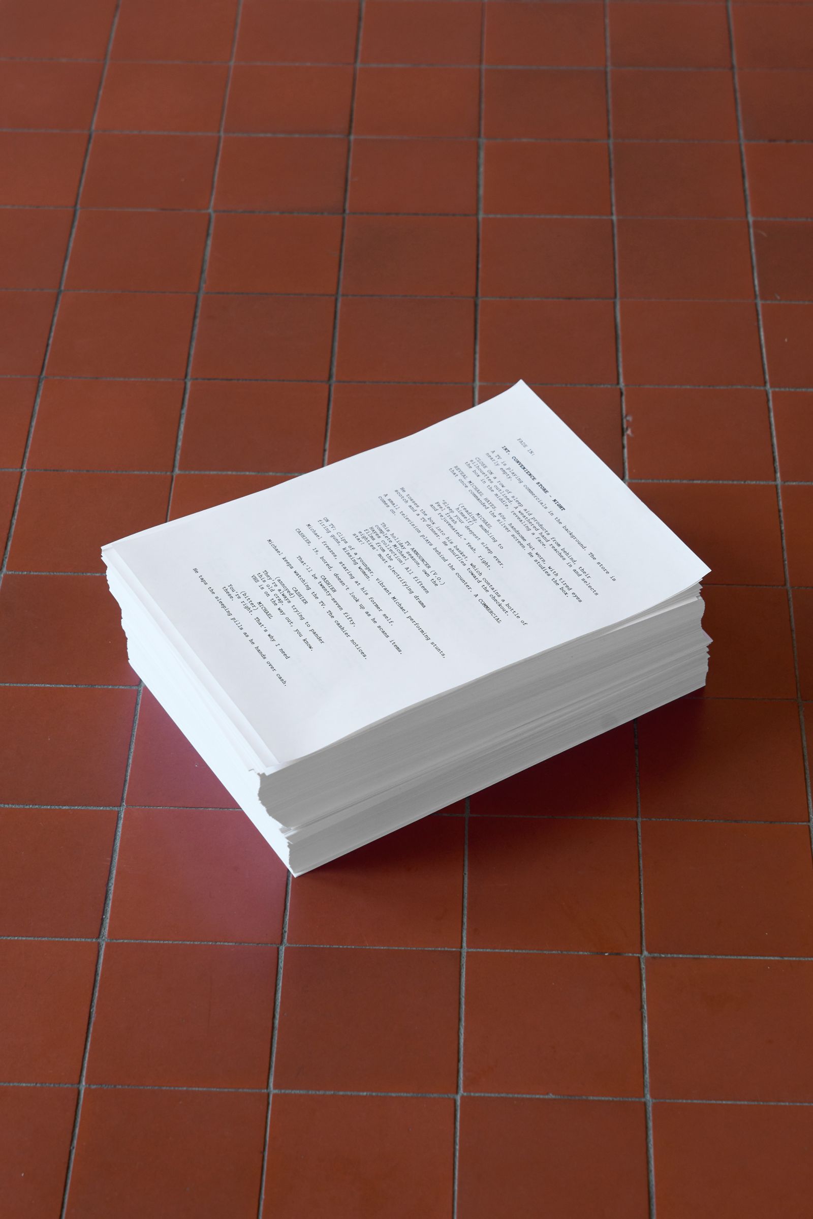 A stack of papers with a screenplay printed on it on a red tiled floor