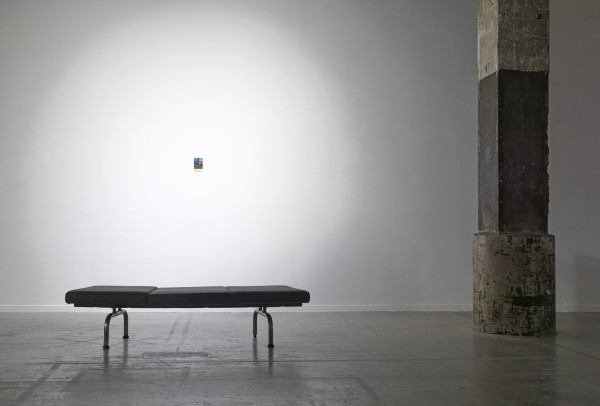 the stupid fish print hangs on a white wall by a bench and a pillar to the right of it, in the scene the print is so small it conveys significance