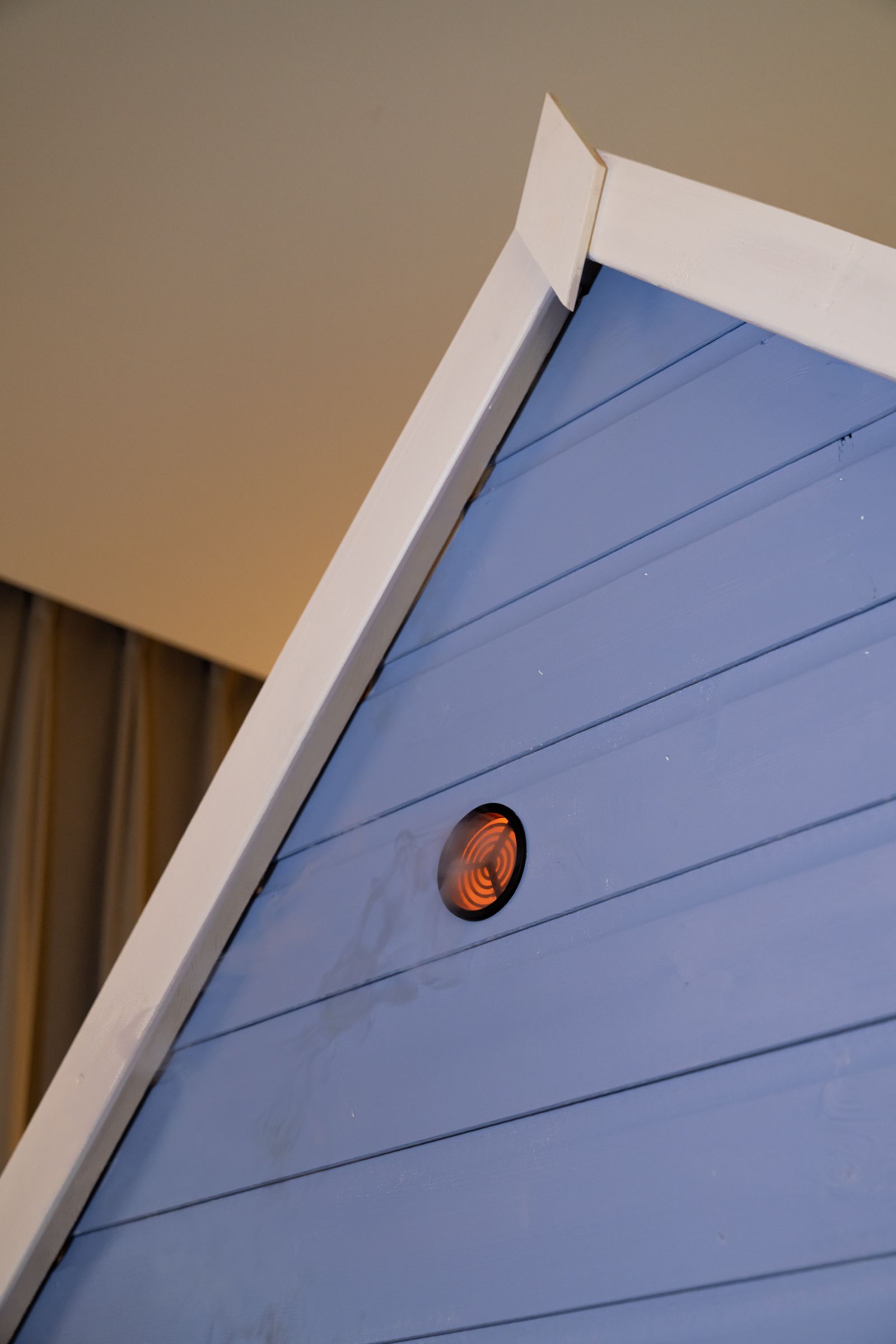 Detail of a blue playhouse roof peak featuring a circular vent with a glowing orange heating element emitting smoke.