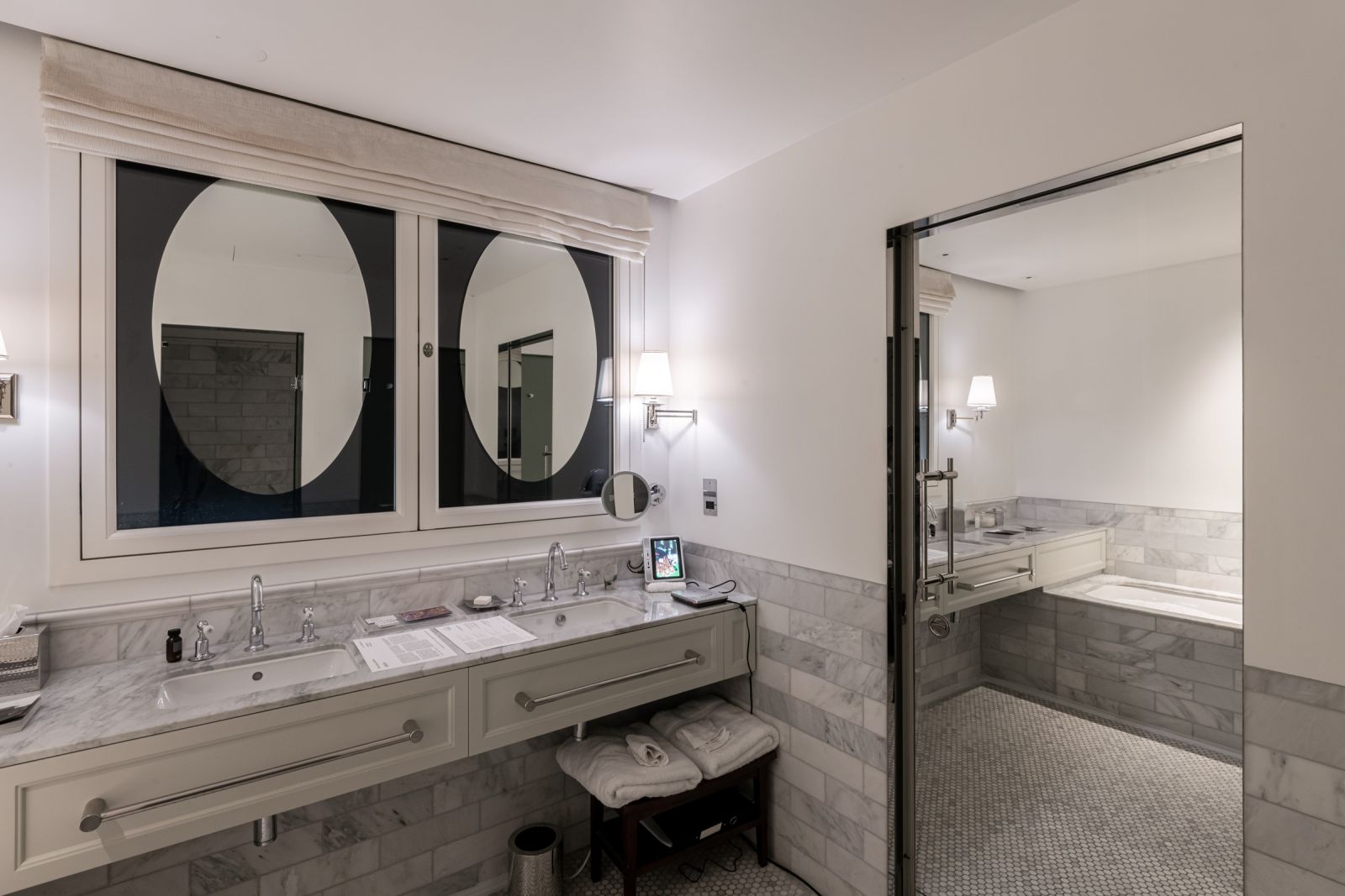 Angled view of a marble bathroom vanity with a portable media player on the counter. Reflection of the snow-filled tub is visible in the large window.