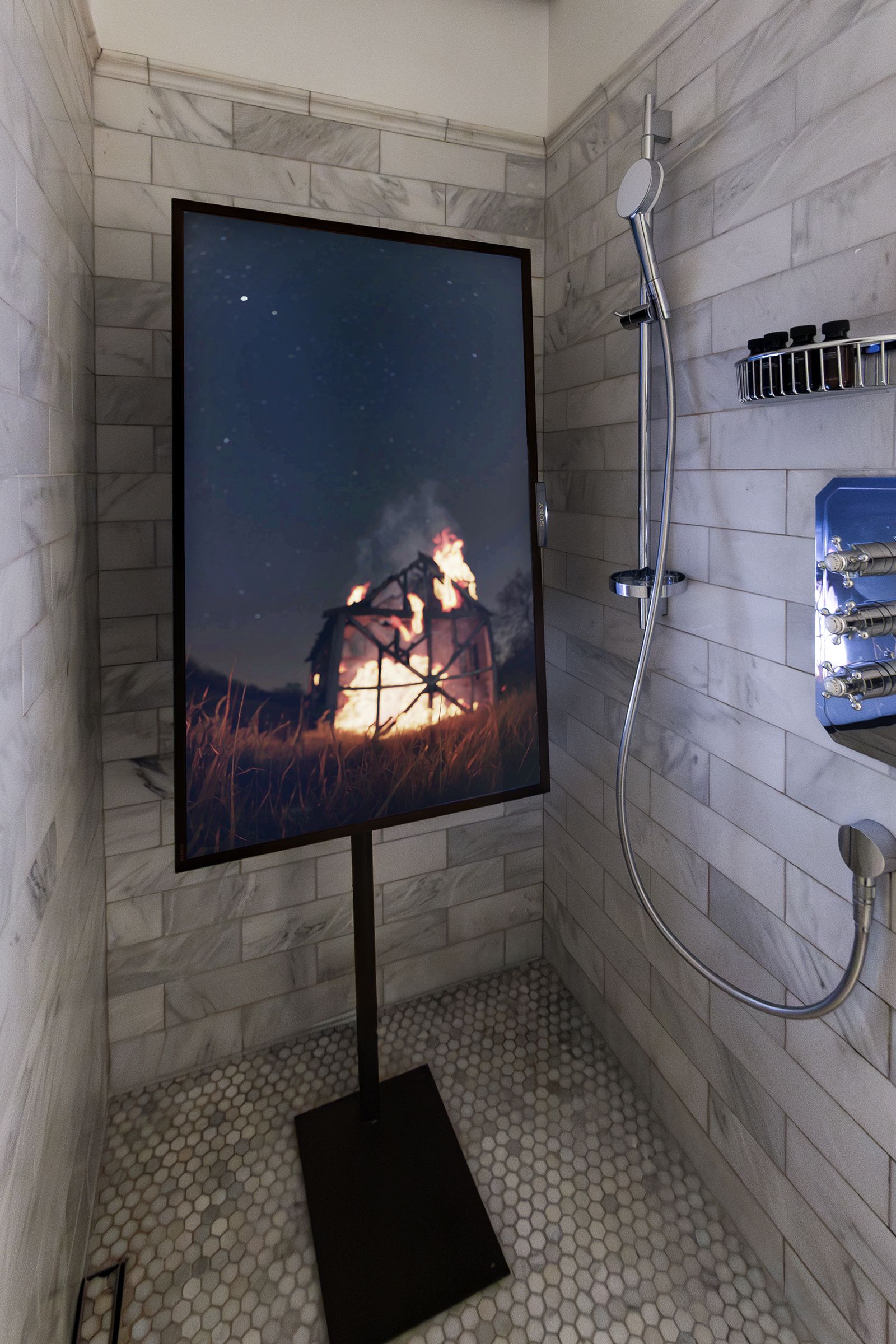 Vertical digital screen positioned in a marble shower stall, displaying an image of a house frame engulfed in flames at night.