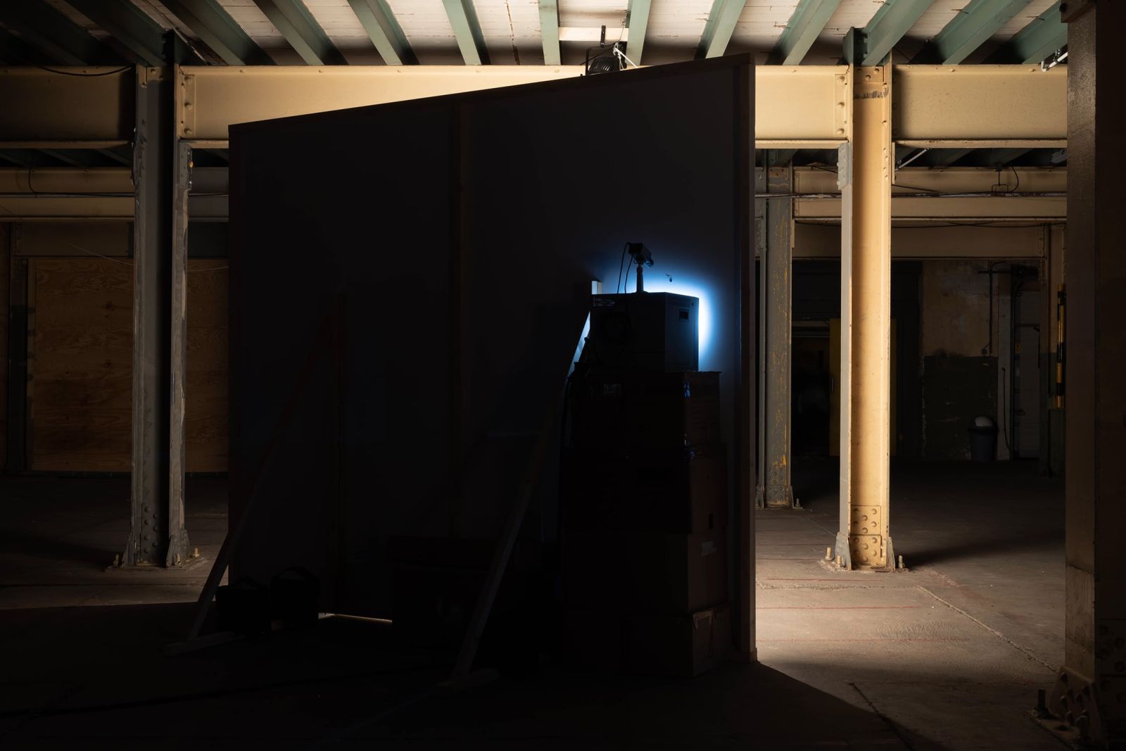 a CRT monitor lights up part of an unlit back of a wall in an industrial space