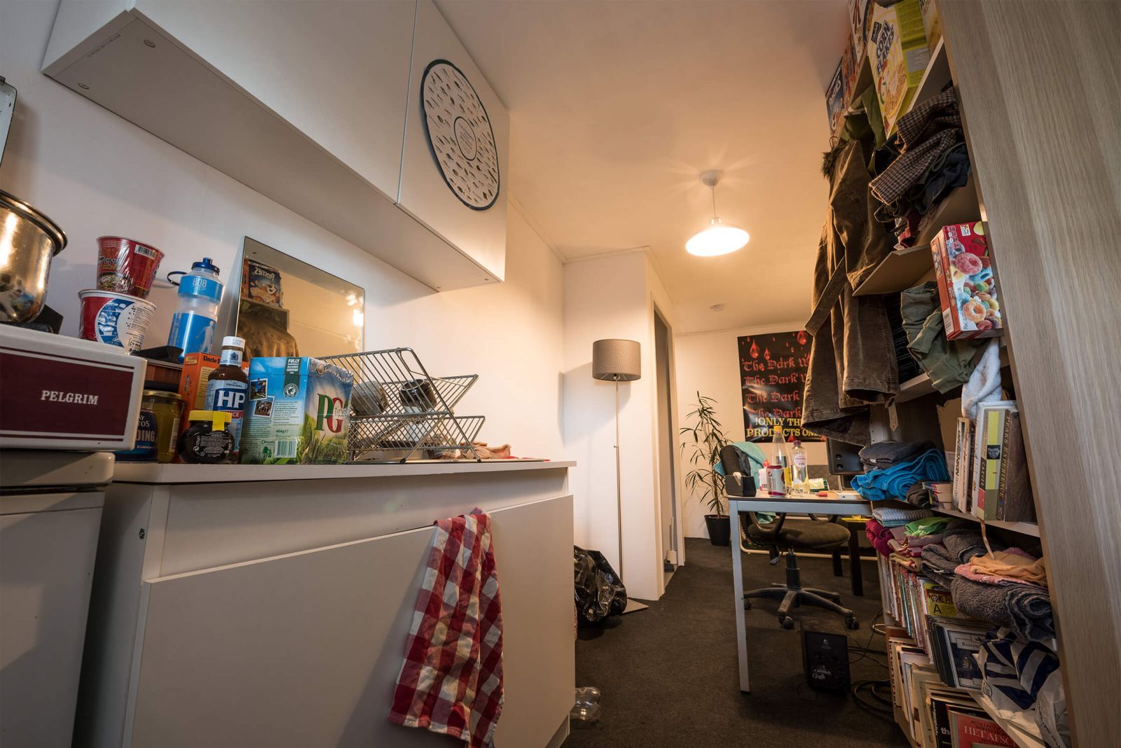 Messy flat interior, white walls, kitchen area, closet with clothes hanging out