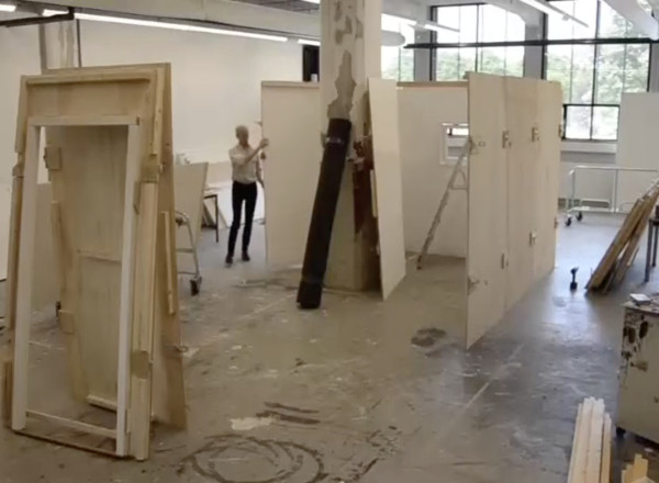 A large industrial room with a person setting up wooden stage walls